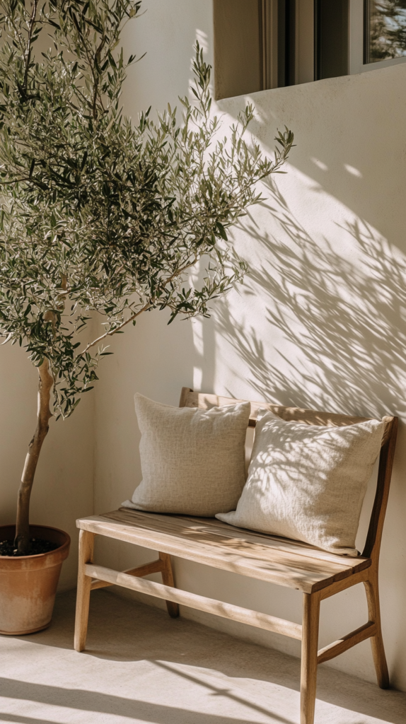 Minimalist balcony with teak bench, olive tree, and linen cushions.